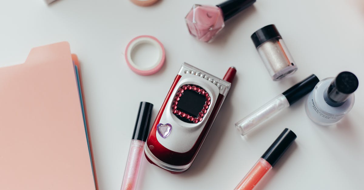 Contact Gloglogirl — flat lay of a vintage flip phone, lip glosses, and neutral makeup