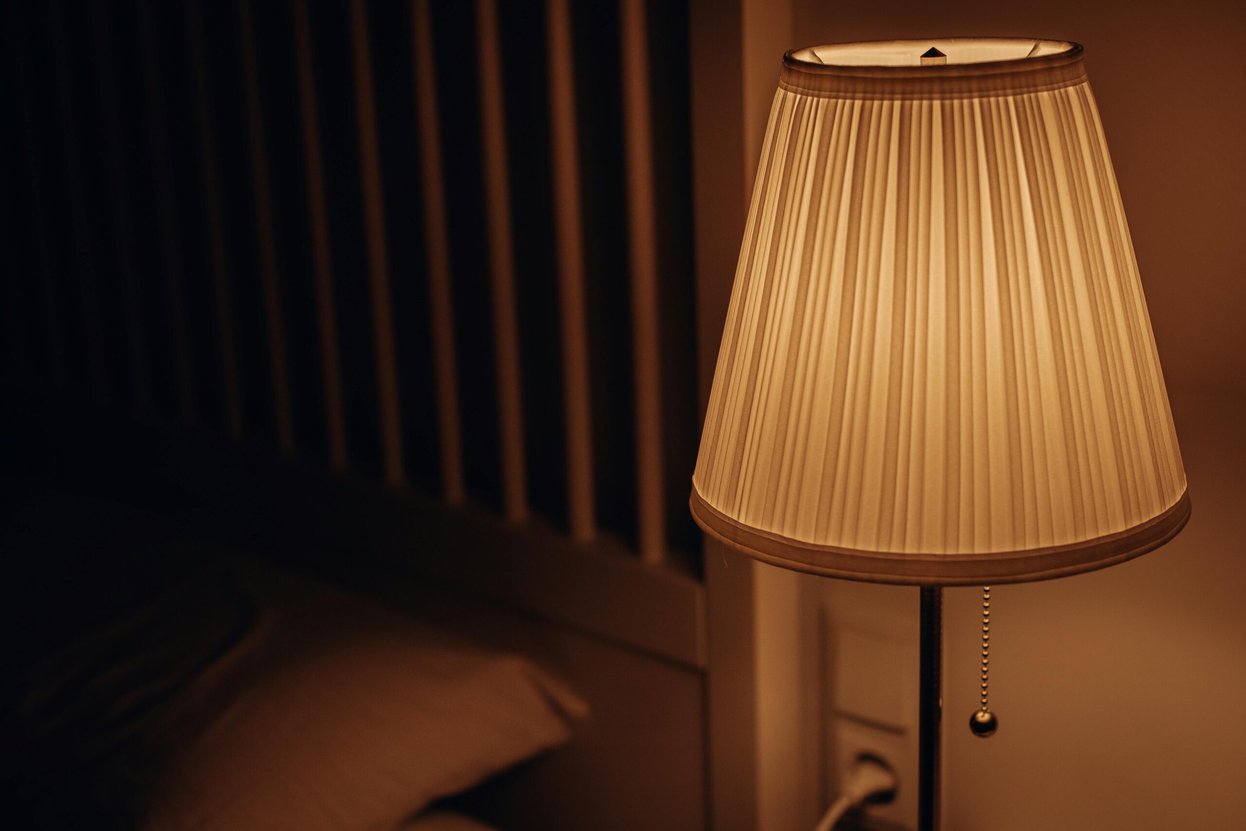 A dimly lit bedside lamp and pillow creating a calm atmosphere — perfect for bedtime habits for better skin