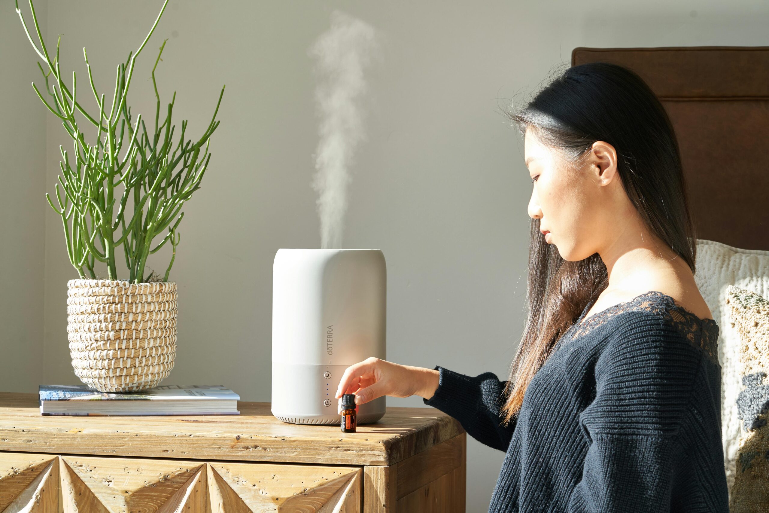 Woman using a cool-mist humidifier in a cozy bedroom to improve skin hydration