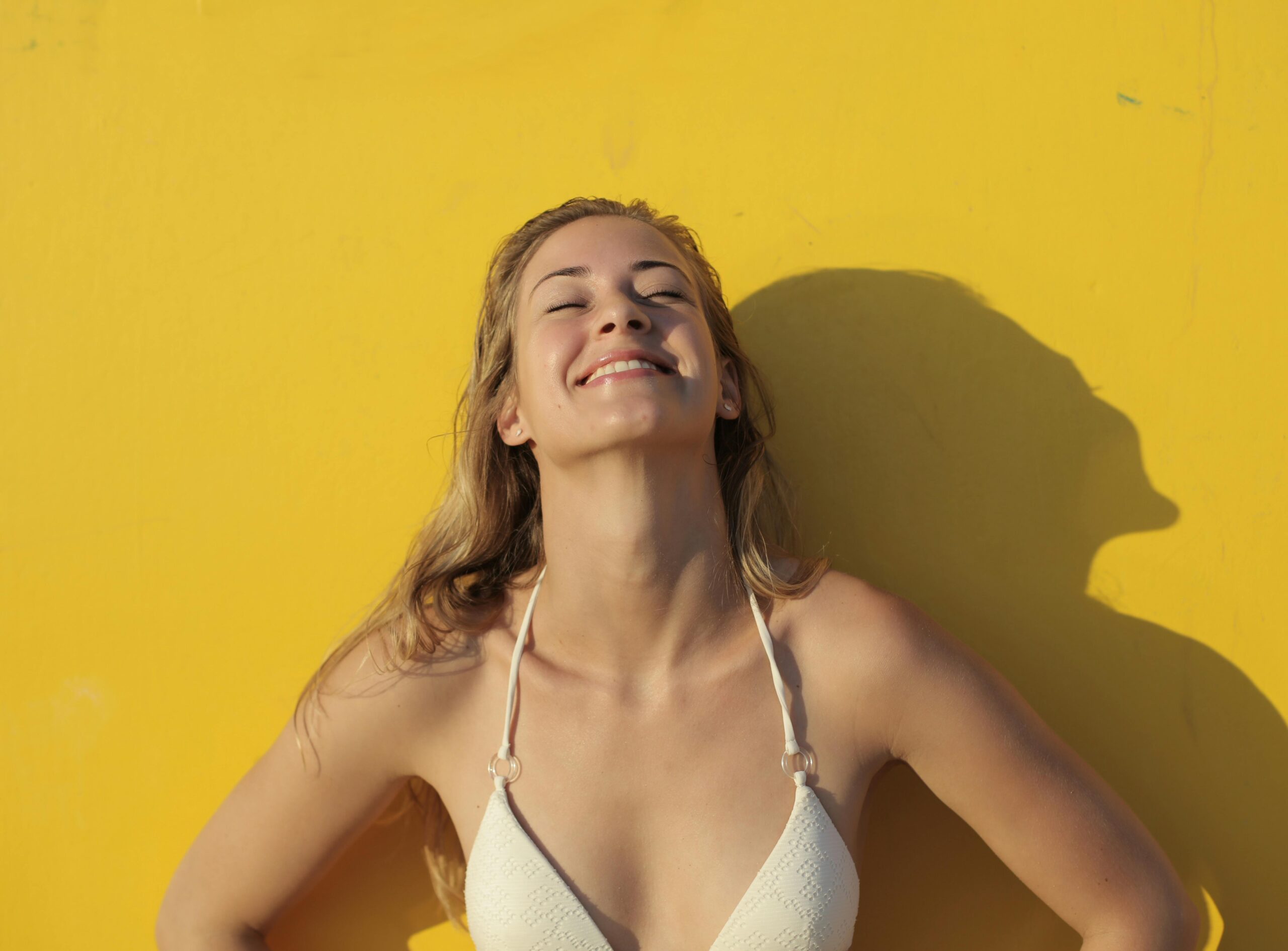 woman smiling in sunlight wearing sunscreen against yellow background – best sunscreen for dry skin Canada